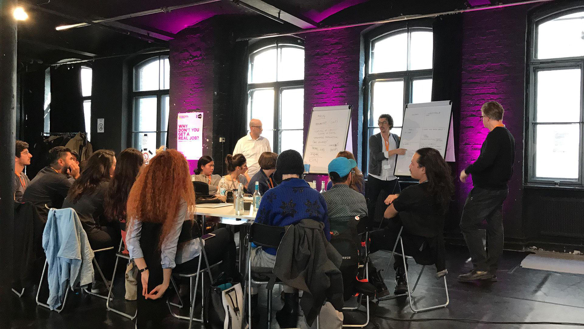 A personal photo from the Berlinale festival World Building workshop, hosted by Alex McDowell and Juan Diaz, showing a small group of people sitting around a table listening to Alex talking