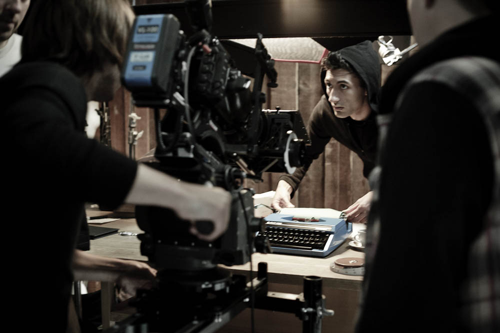 Behind the scenes on The Black Diamond shoot: crew members position a blue vintage typewriter on a wooden desk while a large cinema camera rigs in close, in a darkened studio.