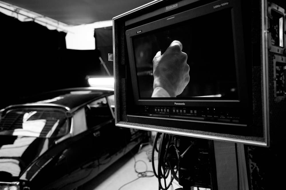 Behind the scenes on The Black Diamond shoot: a Panasonic Filmscape broadcast monitor displays a close-up of a hand in the shot, with the same vintage black car visible behind it in the dark studio.