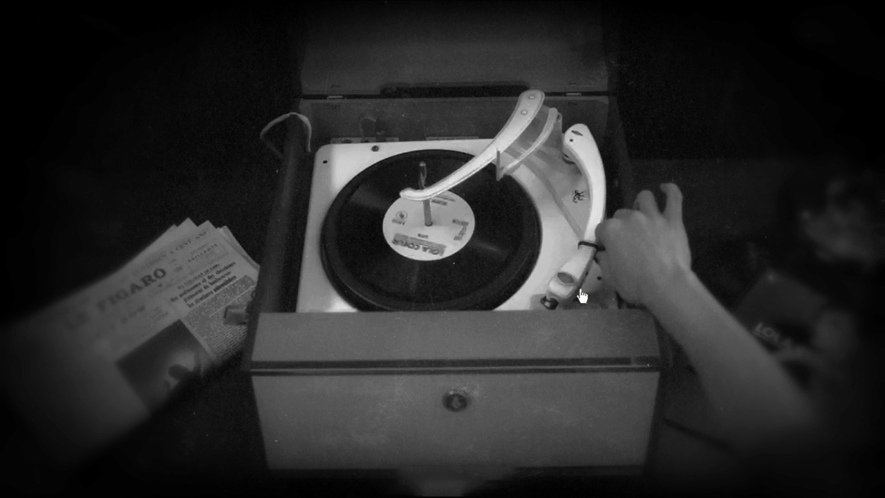 A black-and-white film still from The Black Diamond: a top-down view of a vintage portable record player with a vinyl record spinning, a hand reaching toward the needle, and a folded copy of Le Figaro newspaper visible in the corner.