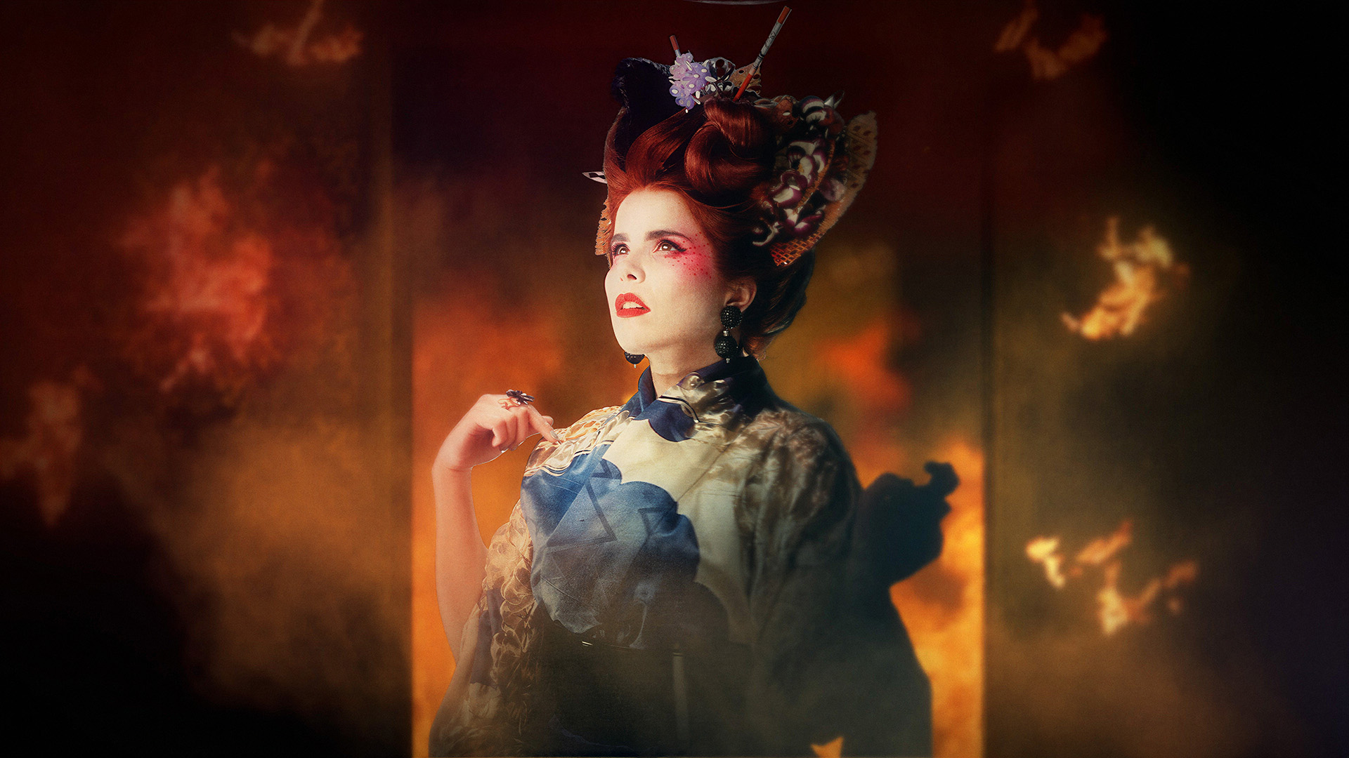 Converse Desire: Paloma Faith in an ornate red hairpiece and patterned robe, lit warmly against a blurred backdrop of flames