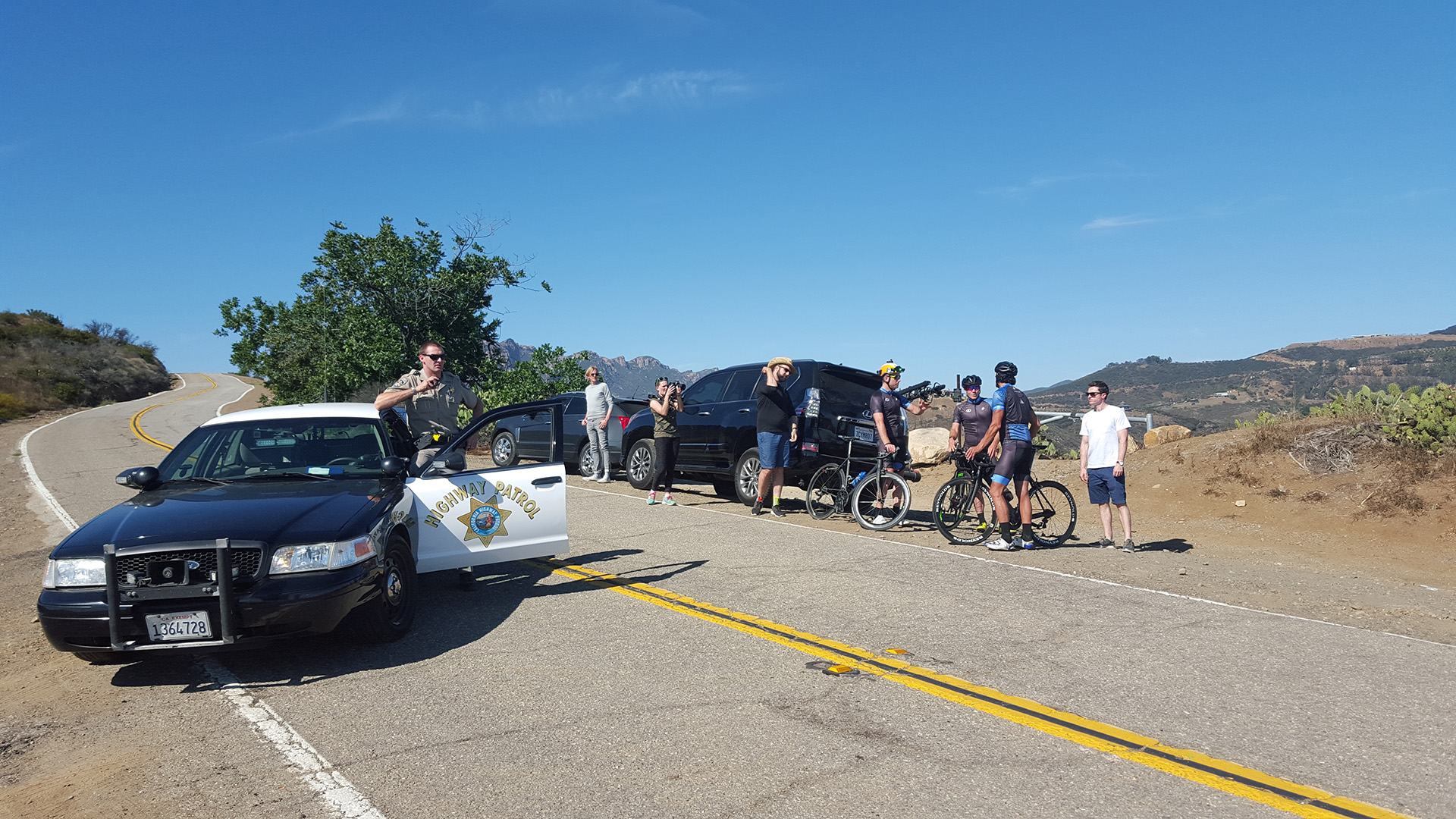 The Elevate film crew gathered on a closed Malibu road with a California Highway Patrol officer, cyclists and production vehicles lined up during a shoot day.