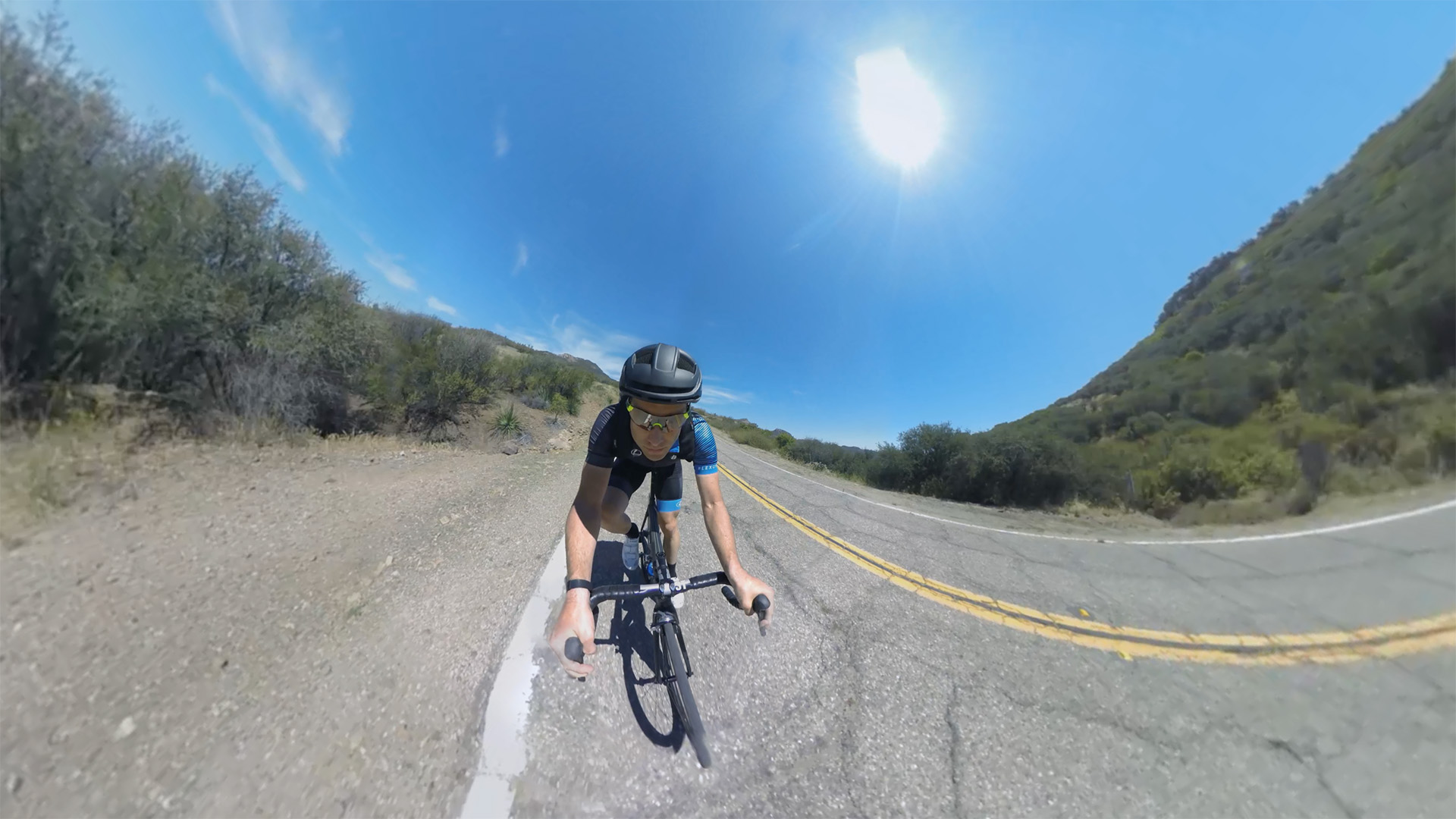 Elevate: Christian Vande Velde in his Lexus cycling kit races directly toward camera on a sun-drenched Malibu road under a blazing midday sun.