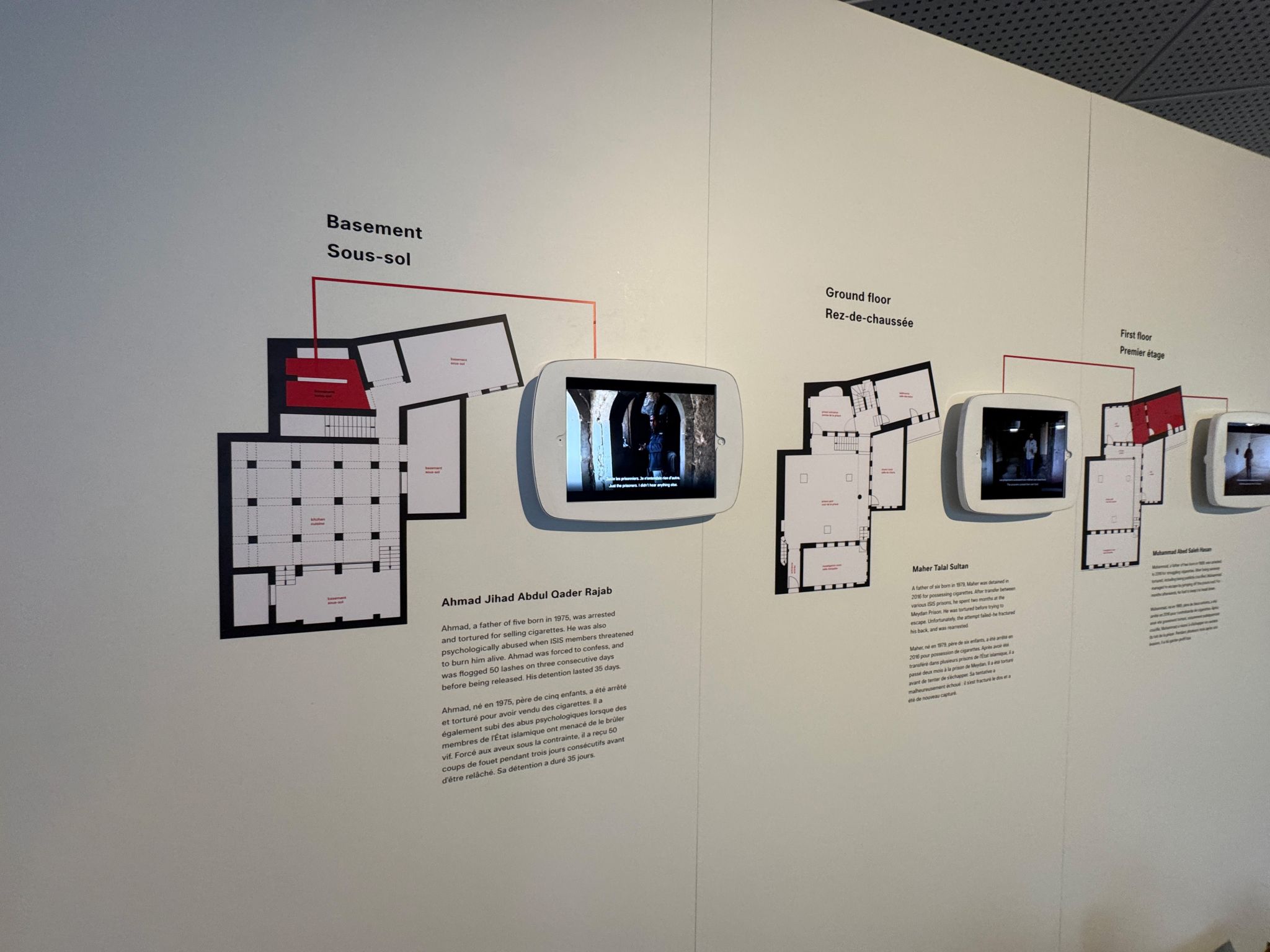 Three iPads on a wall show interviews from Prisoners next to floor plan buildings and descriptive text