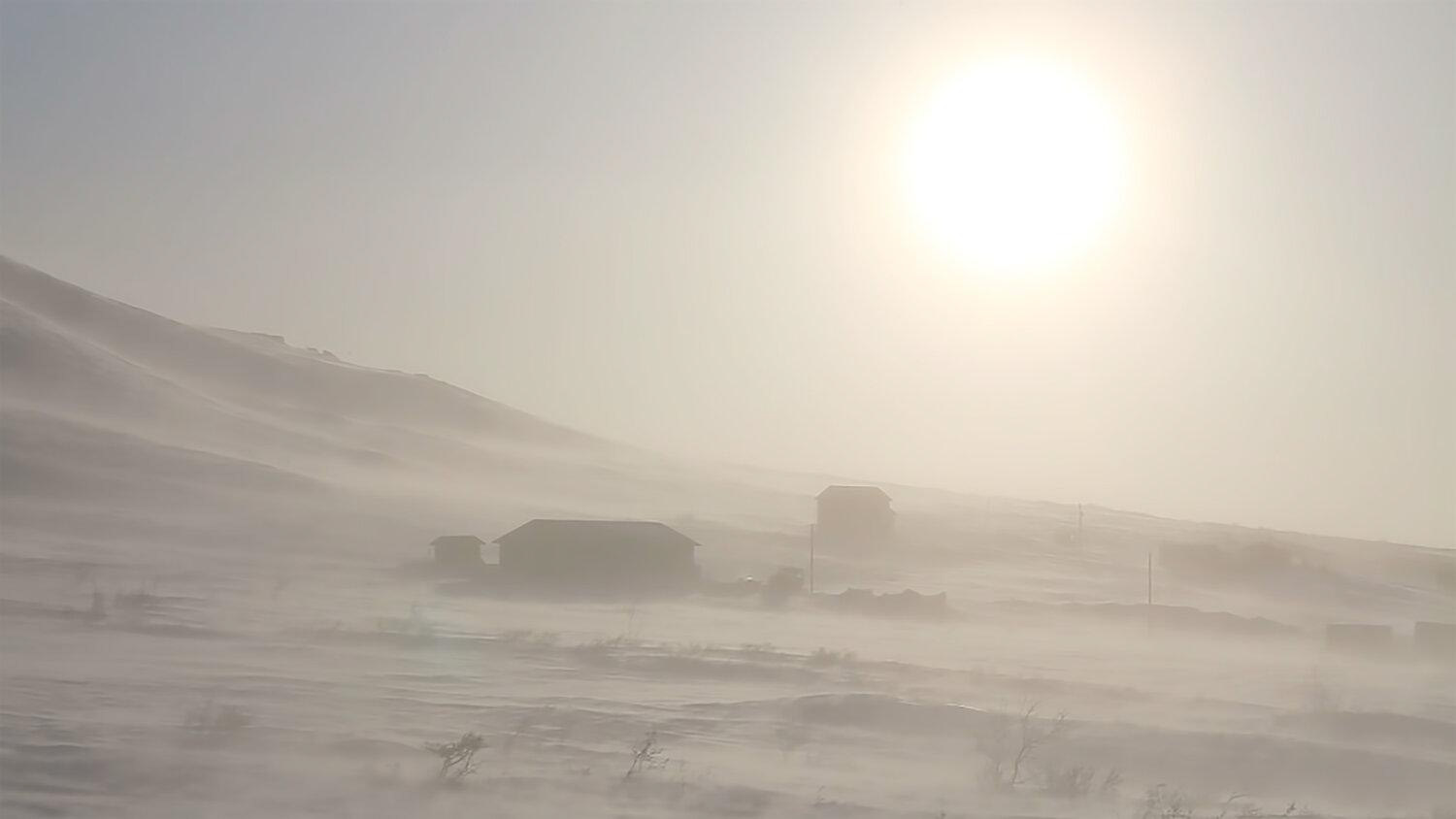 A screenshot of a video of a snowstorm moving over a white landscape, with the sun weakly coming through bathing everything is a yellow light