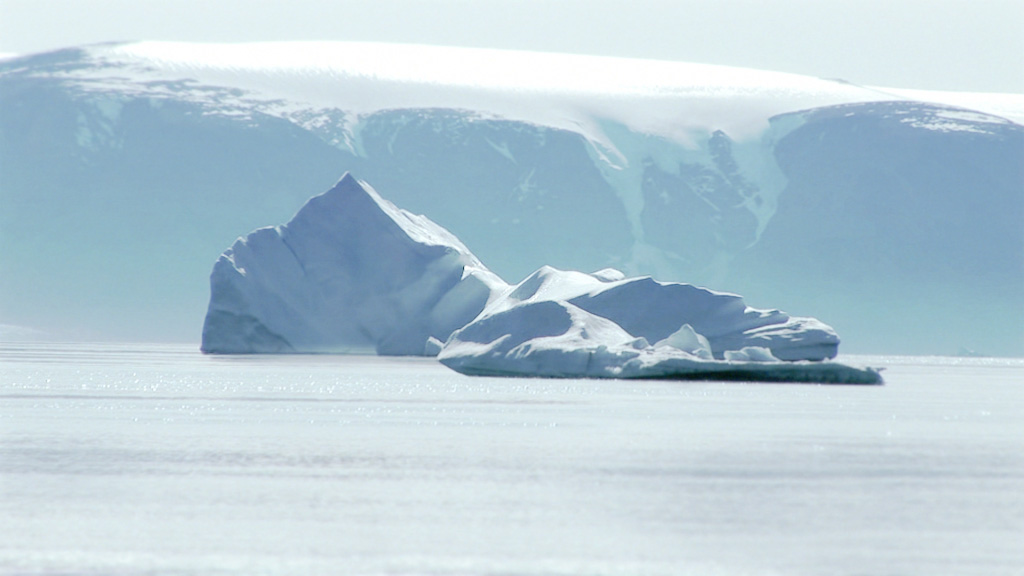 A screenshot showing an ice berg floating in the ocean in the distance