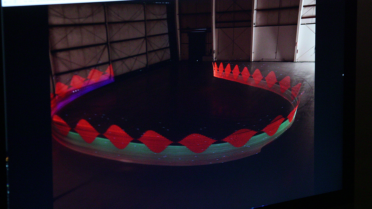 Overhead long-exposure shot of a circular light installation in a dark studio, glowing red and green trails forming a ring on the floor.