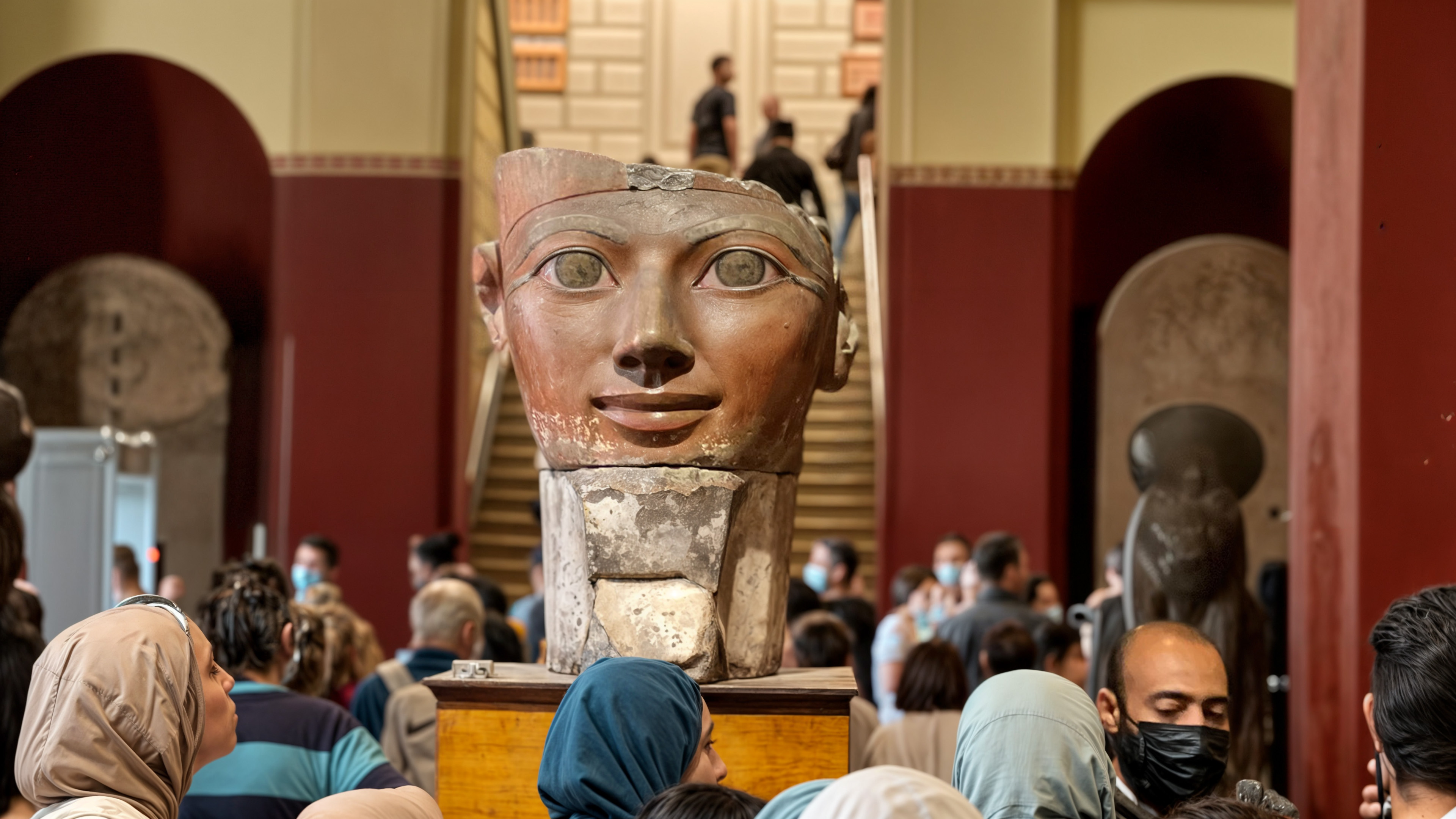 A photo of the head of Hatshepsut, in the Egyptian Museum Cairo, surrounded by a number of visitors who look up and study her