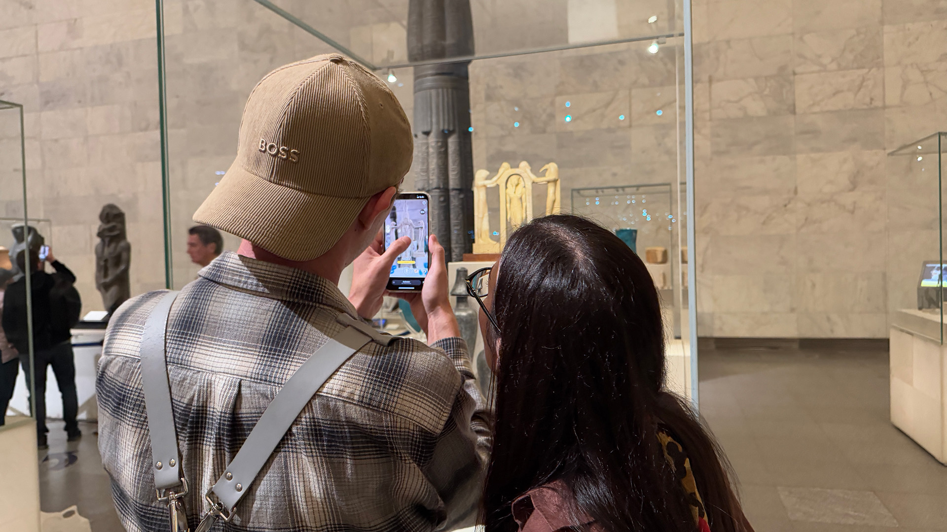 Two visitors use the AR app on a phone to view a small shrine-shaped artefact in a display case.