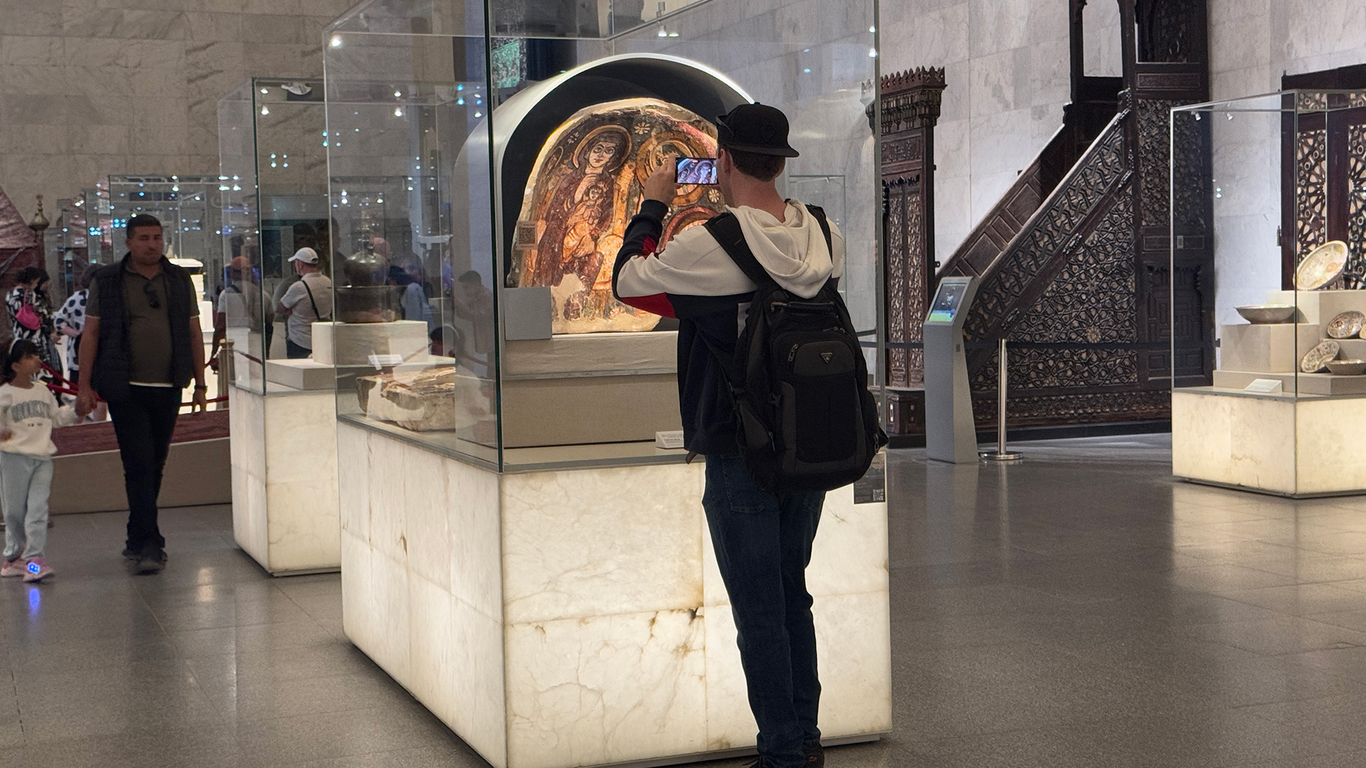 A visitor uses his phone to view the AR app over a painted Coptic wall fragment displayed in an arched case.