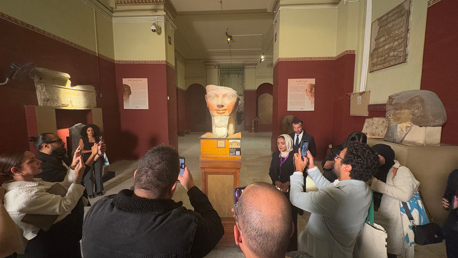 Museum visitors photograph a large carved head of Hatshepsut on a plinth in a gallery of the Egyptian Museum.