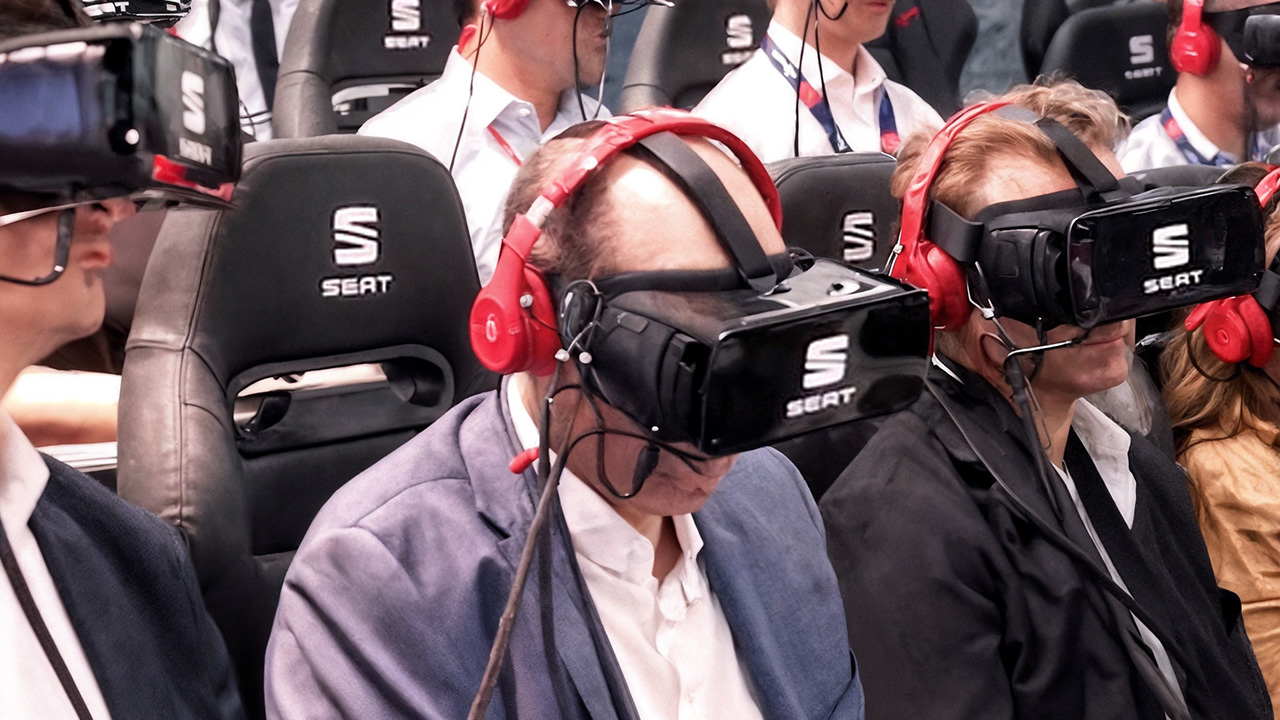 Audience members seated in branded SEAT car seats wearing VR headsets and red headphones during the Seat 4D immersive experience. The group is engaged in a synchronized virtual reality presentation, combining motion seating with audio-visual immersion to simulate the feeling of being inside a SEAT vehicle.