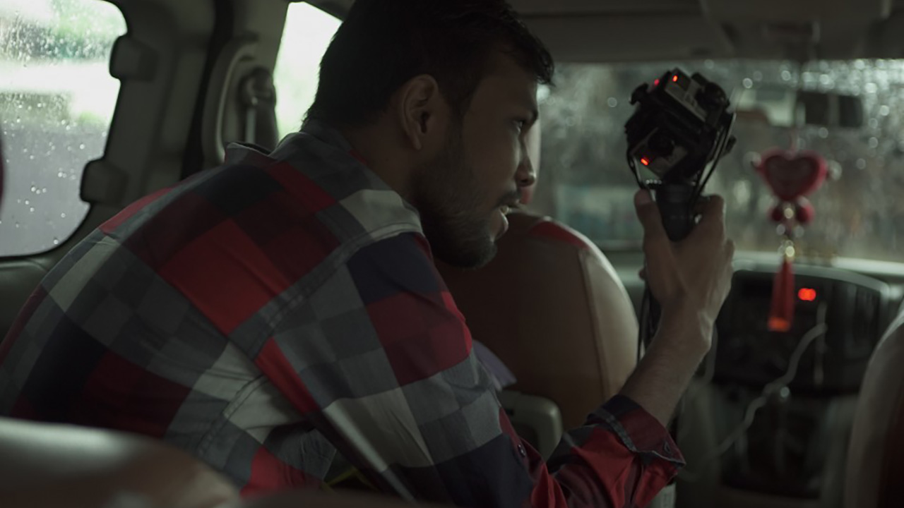THE RETURN: A crew member holds a rigged 360° camera up to a rain-streaked car window, filming from inside the vehicle.