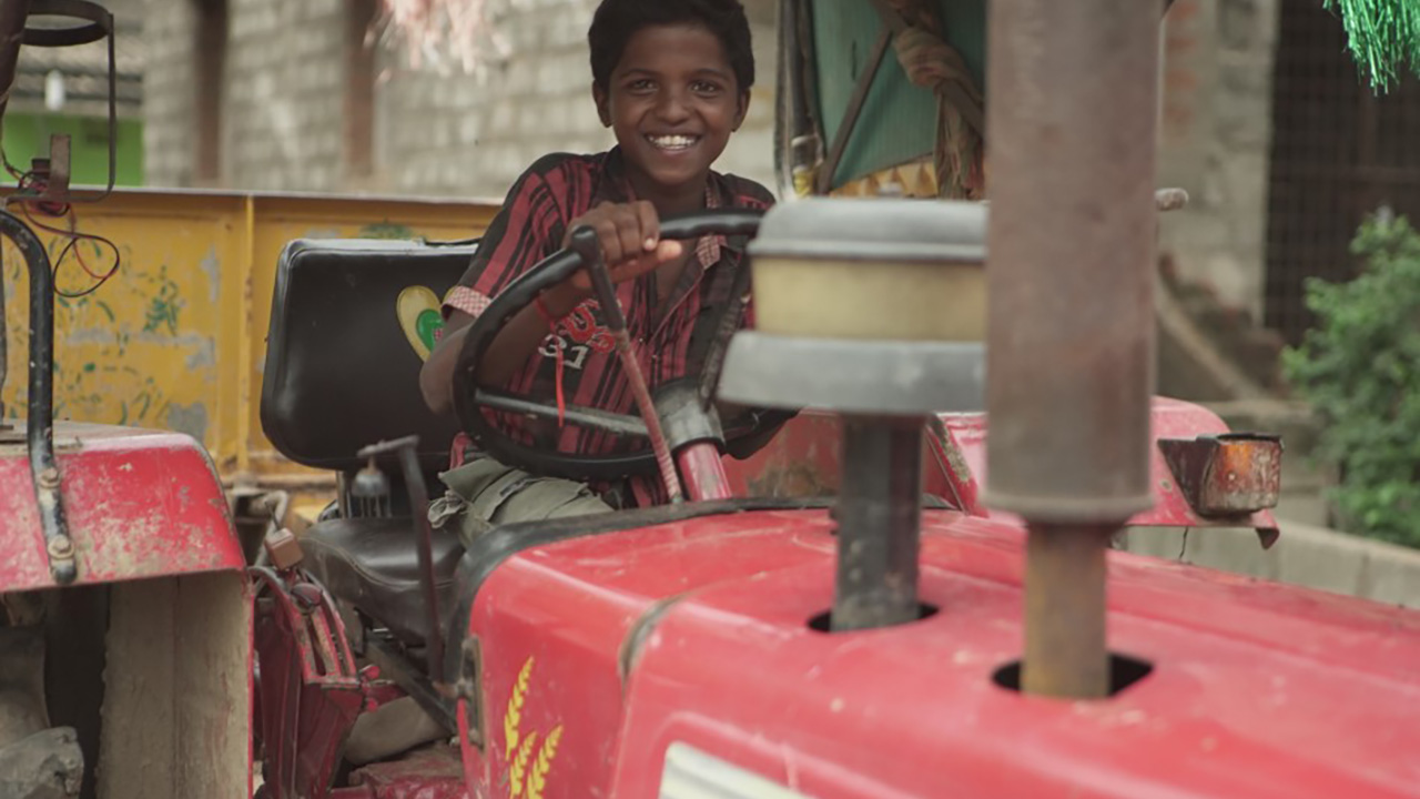 THE RETURN: A boy smiles from the driver's seat of a red tractor.