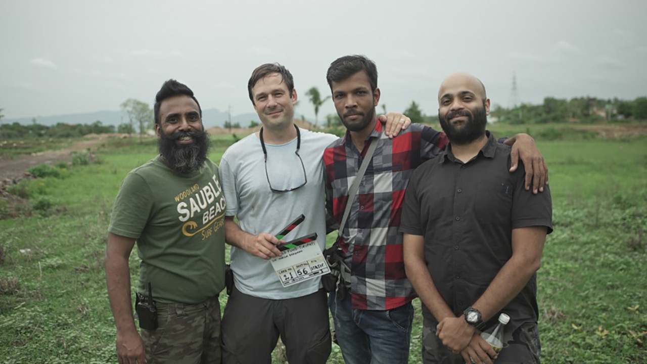 THE RETURN: Four crew members pose together in a green field, one holding a clapperboard.