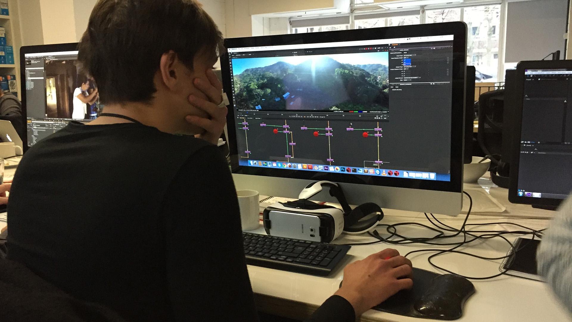 WATER: An editor reviews 360° drone footage of green hills in a video editing timeline, a VR headset resting on the desk beside the keyboard.